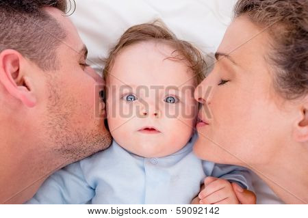High angle of loving parents kissing baby boy in bed