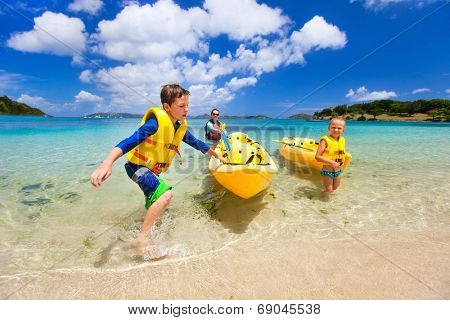 Family with kids paddling on colorful yellow kayaks at tropical ocean water during summer vacation
