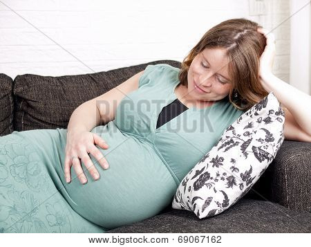 Pregnant Young Woman Resting On The Couch While Holding Her Belly