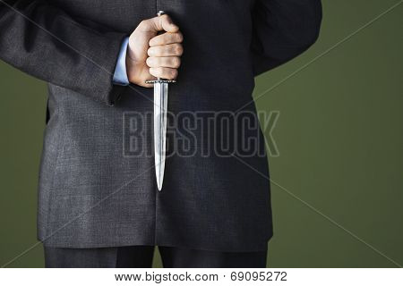 Closeup midsection of a businessman holding knife behind back against green background
