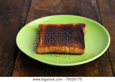 Burnt toast bread on light green plate, on wooden table background