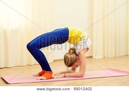 Slender athletic girl doing yoga exercises indoor. Backbend.
