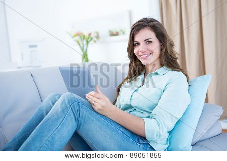 Happy brunette using her tablet pc on couch at home in the living room