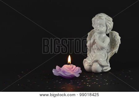 Beautiful statue of an angel near a lit candle on black background