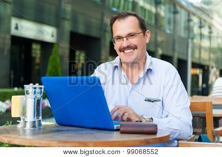 Middle age smiling businessman works on laptop in outdoor cafe