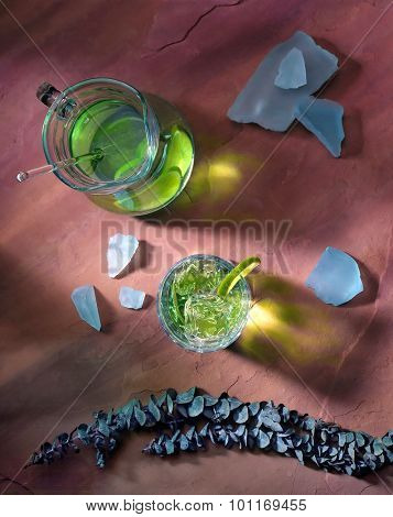 High angle shot of a pitcher of lime ade on a red sandstone background. 