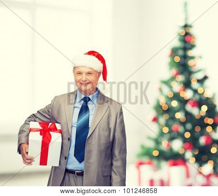 business, christmas, xmas, happiness concept - smiling old man in suit and santa helper hat with gift