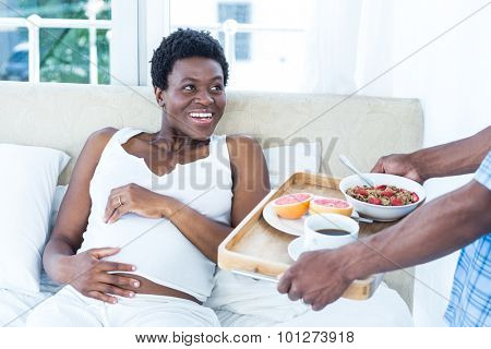 Pregnant woman smiling while looking at man bringing breakfast at home