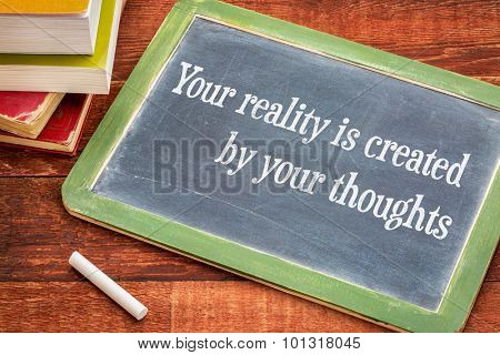 Your reality is created by your thoughts - inspirational phrase on slate blackboard with a white chalk and a stack of books against rustic wooden table