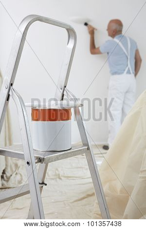 Man Decorating Room With Can Of Paint And Brush In Foreground