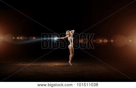 Hot young dancing woman in white bikini on dark background