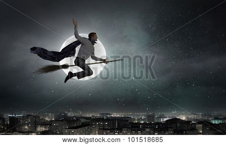 Young businessman flying on broom high in sky
