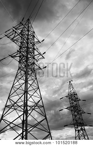 High voltage electricity pylons against rainy cloud.