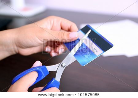 Woman's hands cutting bank card with scissors on wooden table background