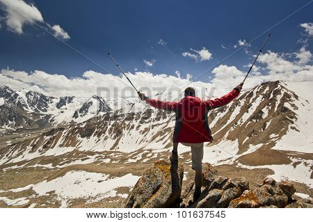 man standing on a cliff in mountains with poles