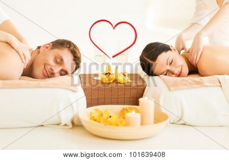 spa, beauty, love and happiness concept - smiling couple with candles, flowers and champagne glasses getting massage in spa salon