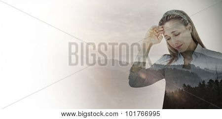 Upset woman touching forehead against trees and mountain range against cloudy sky
