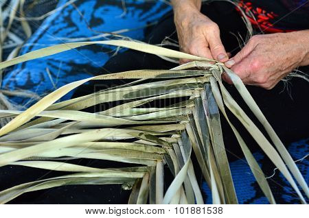Hands of an old Maori woman weaving a traditional Maori woven artwork.