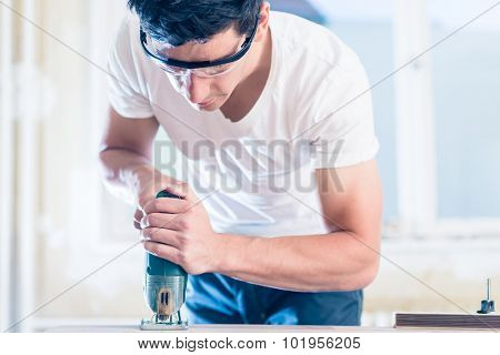 DIY worker cutting wooden panel with jig saw
