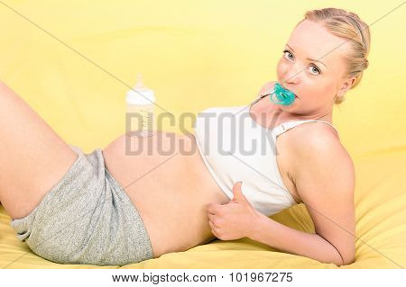Pregnant Woman Holding Baby Bottle At The Belly Lying In Her Sleeping Room At Home