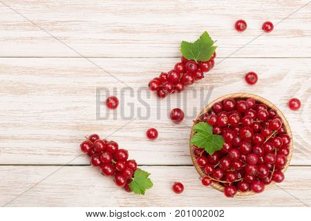 Red currant berries in a wooden bowl with leaf on the light wooden background with copy space for your text. Top view.