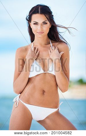 Sexy brunette girl in white swimsuit posing on a beach