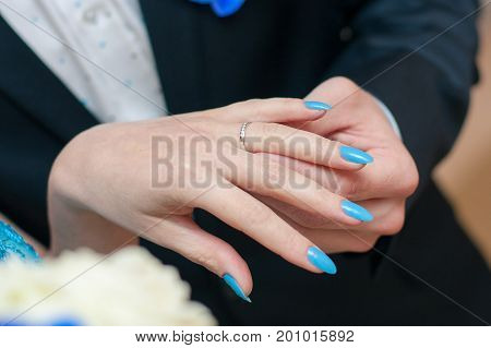 The groom puts a wedding ring on bride's finger with 
blue manicure, gently. Macro frame of hands newlyweds.