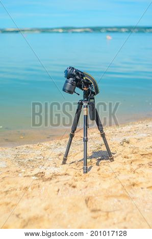 Camera on a tripod near the seaside removes of seashells on the sand. Photographic equipment in the process of shooting the landscape. Camera while taking a photo or time-lapse
