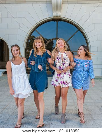 Pretty college girls together in a group walking in white brick courtyard with arms linked.