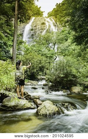 Travel and freedom. Young woman in selfie with backpack enjoying tropical waterfall view.