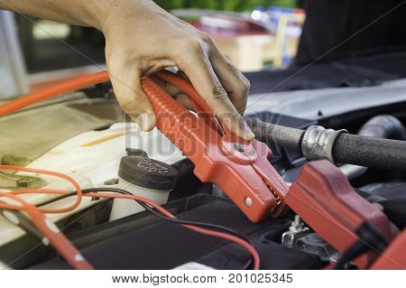 Auto mechanic uses a charging battery with electricity trough jumper cables in a carSelective focus.
