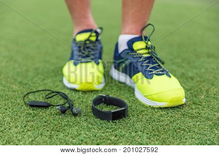 Fitness sport wearable devices man wearing running shoes with wireless earbuds, smartwatch lying on grass floor. Tech run gear, smart watch and earphones for runners.