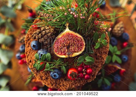 From above view of few levels cake topped with berries fruit and twigs.