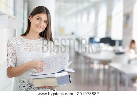 Pretty, young college student looking for a book in the library, studying for her exam