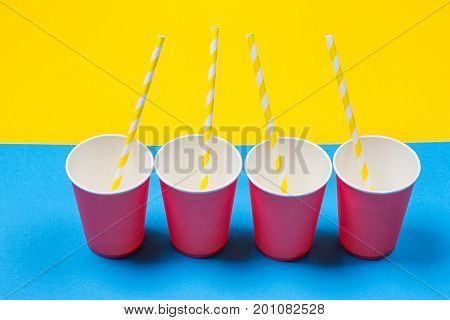 a bundle of multi-colored drinking straws in a paper Cup on a yellow and blue background. fashion minimal. flat lay
