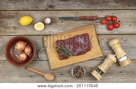A piece of raw meat, rosemary and spices on the kitchen table
