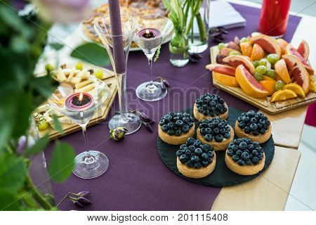 Blueberry tartlets on slate stone, plate with fruits, candles. Sweet dishes on the table. Romantic supper.