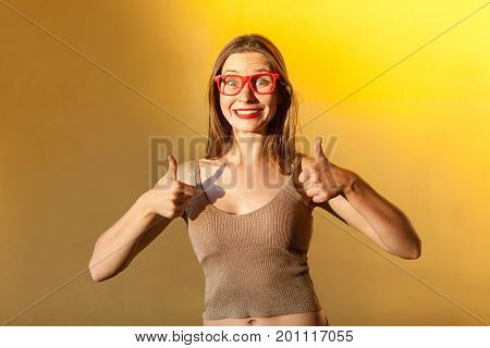 Like it! Femininity attractive girl with glasses thumbs up toothy smile and looking at camera. Yellow background. Studio shot