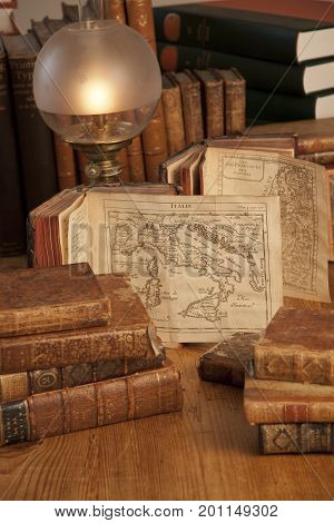 Vintage, antiquarian books pile on wooden surface in warm light with old world maps. Copenhagen, August 14, 2010