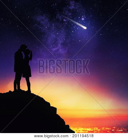 Couple of lovers in backlight from above a mountain expresses a desire during the sight of a falling star