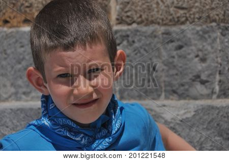 A gloomy boy with milk teeth in a shirt and a bandage laughing on a sunny day.