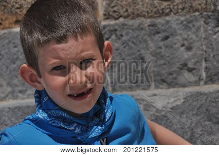 A gloomy boy with milk teeth in a shirt and a bandage laughing on a sunny day.