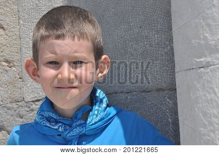 A gloomy boy with milk teeth in a shirt and a bandage laughing on a sunny day.