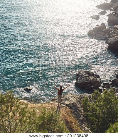 Back view of woman standing on the sea coast Between pines and Enjoying the sunset