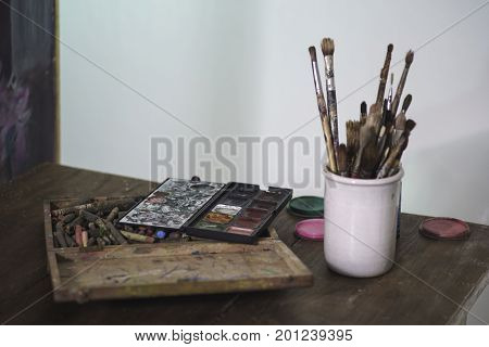 Some brushes and colors in a vintage Location ower a wooden table.