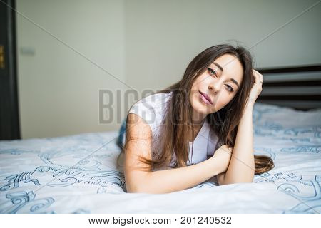 Woman Lying At The End Of The Bed Looking Forward And Smiling. Her Hand Against Her Chin With Her Ot