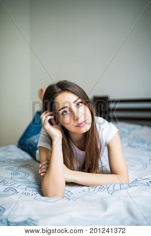 Young Woman Lying At The End Of The Bed Smiling, With Her Head Resting Upon Her Hand With The Other
