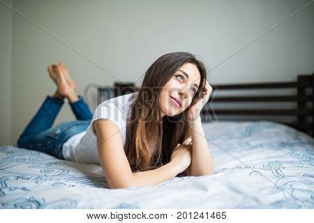 Young Woman Lying At The End Of The Bed Smiling, With Her Head Resting Upon Her Hand With The Other