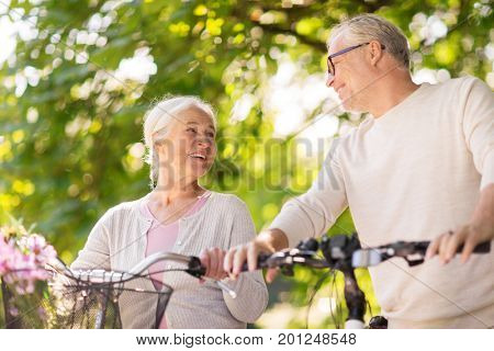 old age, people and lifestyle concept - happy senior couple walking with fixie bicycles talking at summer city park