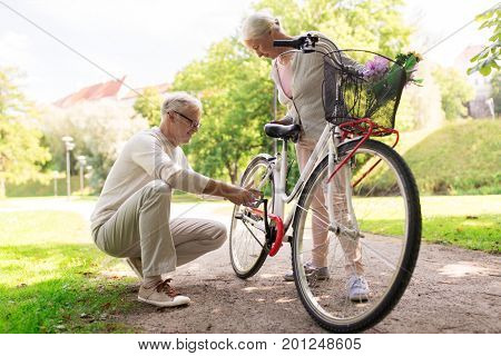 old age, people and lifestyle concept - happy senior couple with fixie bicycle at summer city park